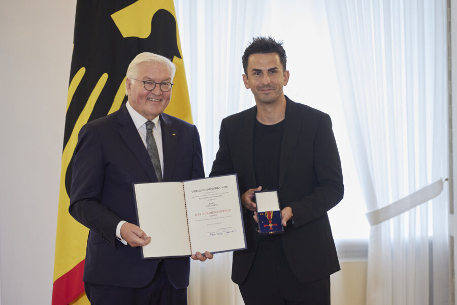 Zwei Männer mit Urkunde und Auszeichnung, Deutschlandflagge im Hintergrund.