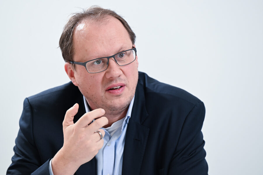 Person mit Brille und Anzug spricht und gestikuliert.