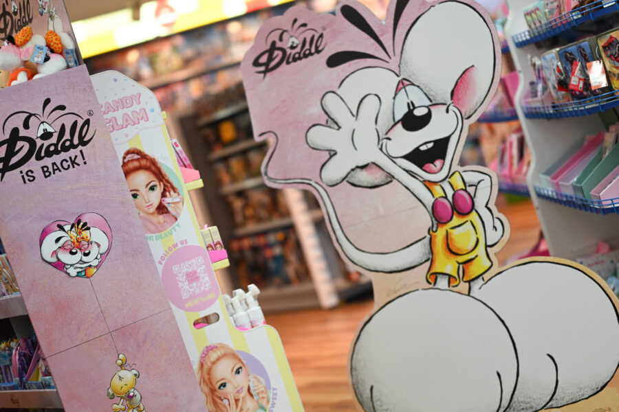 Pappfigur einer weißen Comic-Maus in gelber Latzhose in einem Laden.