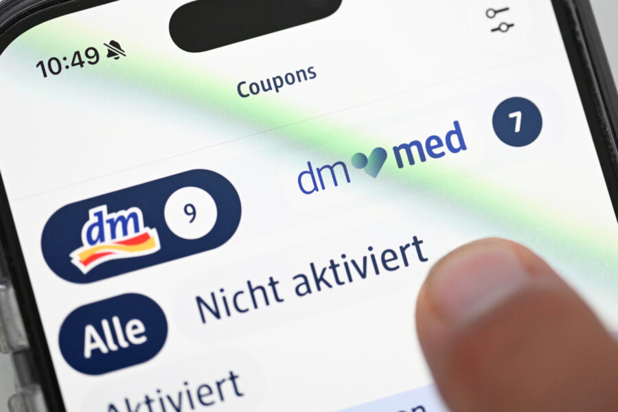 Smartphone zeigt App mit „Coupons“, „dm 9“ und „Nicht aktiviert“. Finger tippt.