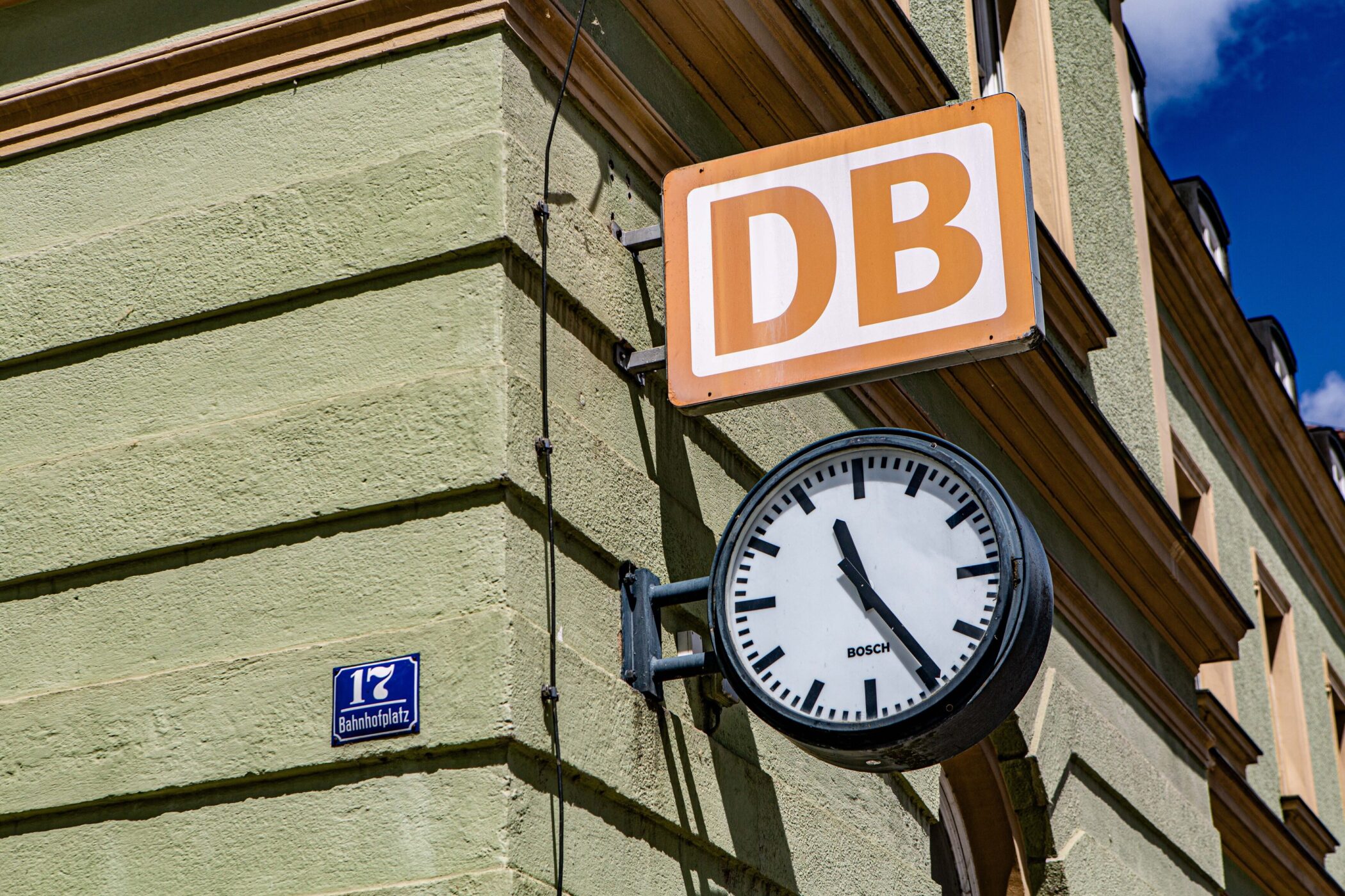 Wanduhr und DB-Schild an grüner Hauswand, Schild mit "Bahnhofplatz 17".