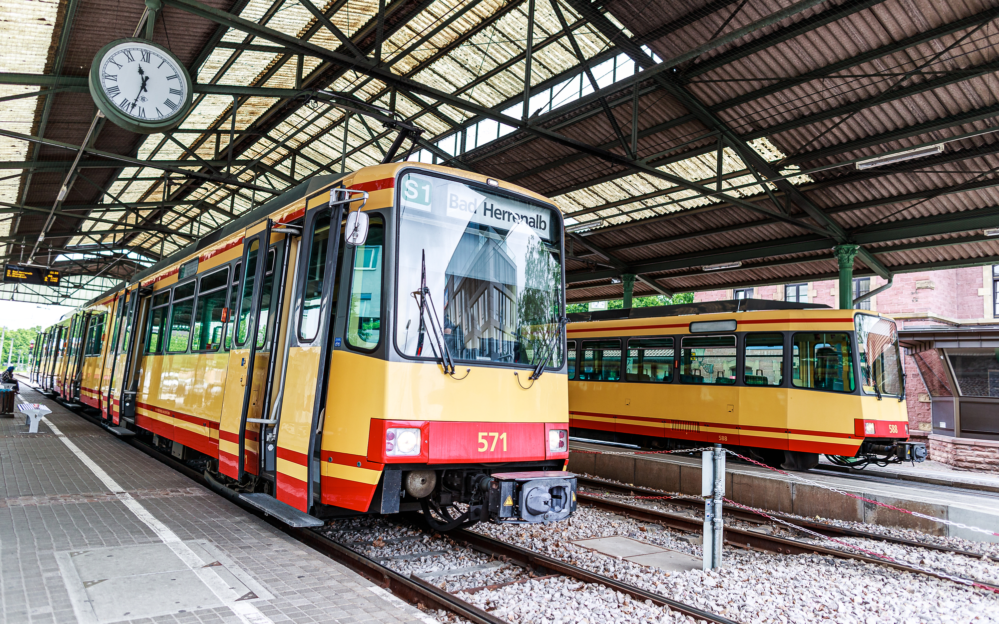 Zwei gelbe Straßenbahnen im Bahnhof unter einem Uhrendach.