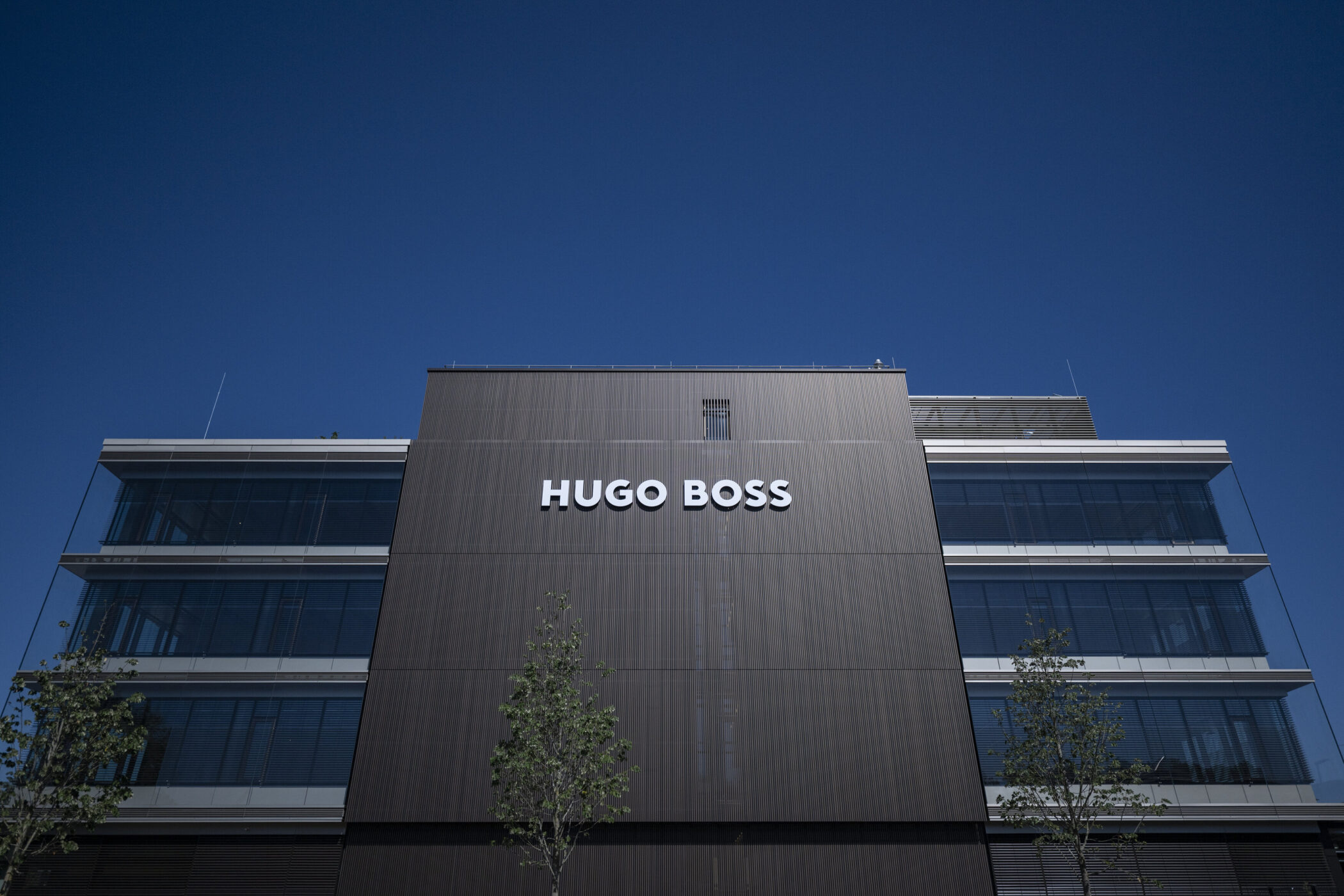Gebäude mit "HUGO BOSS"-Schriftzug und Glasfronten, blauer Himmel.