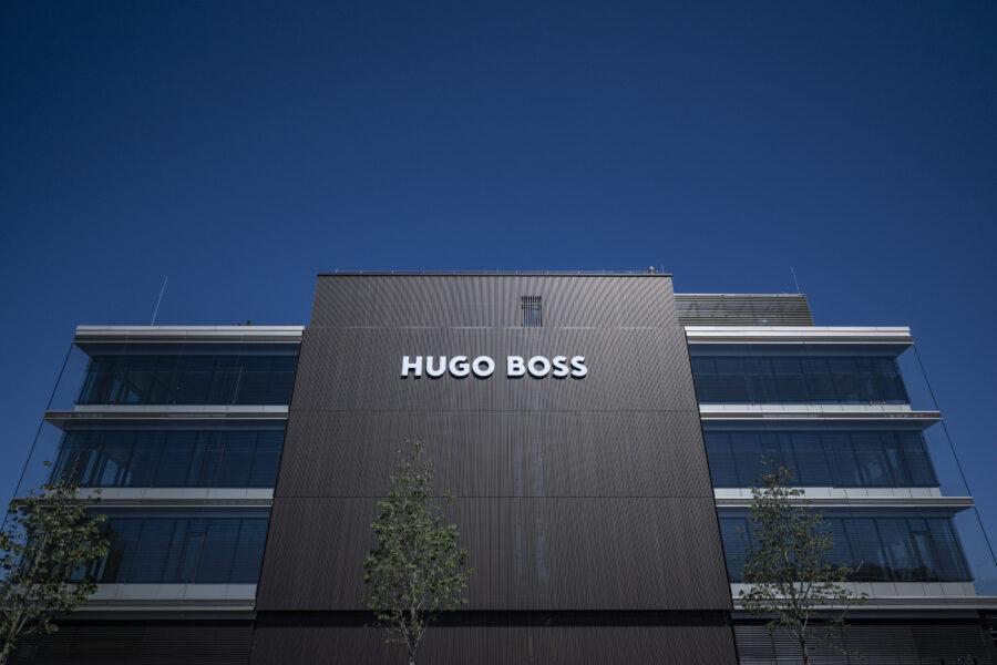 Gebäude mit "HUGO BOSS"-Schriftzug und Glasfronten, blauer Himmel.