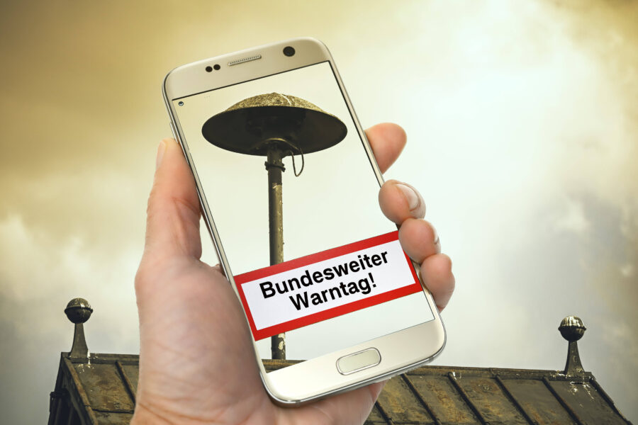 Hand hält Handy mit Bild einer Sirene, Text „Bundesweiter Warntag!“