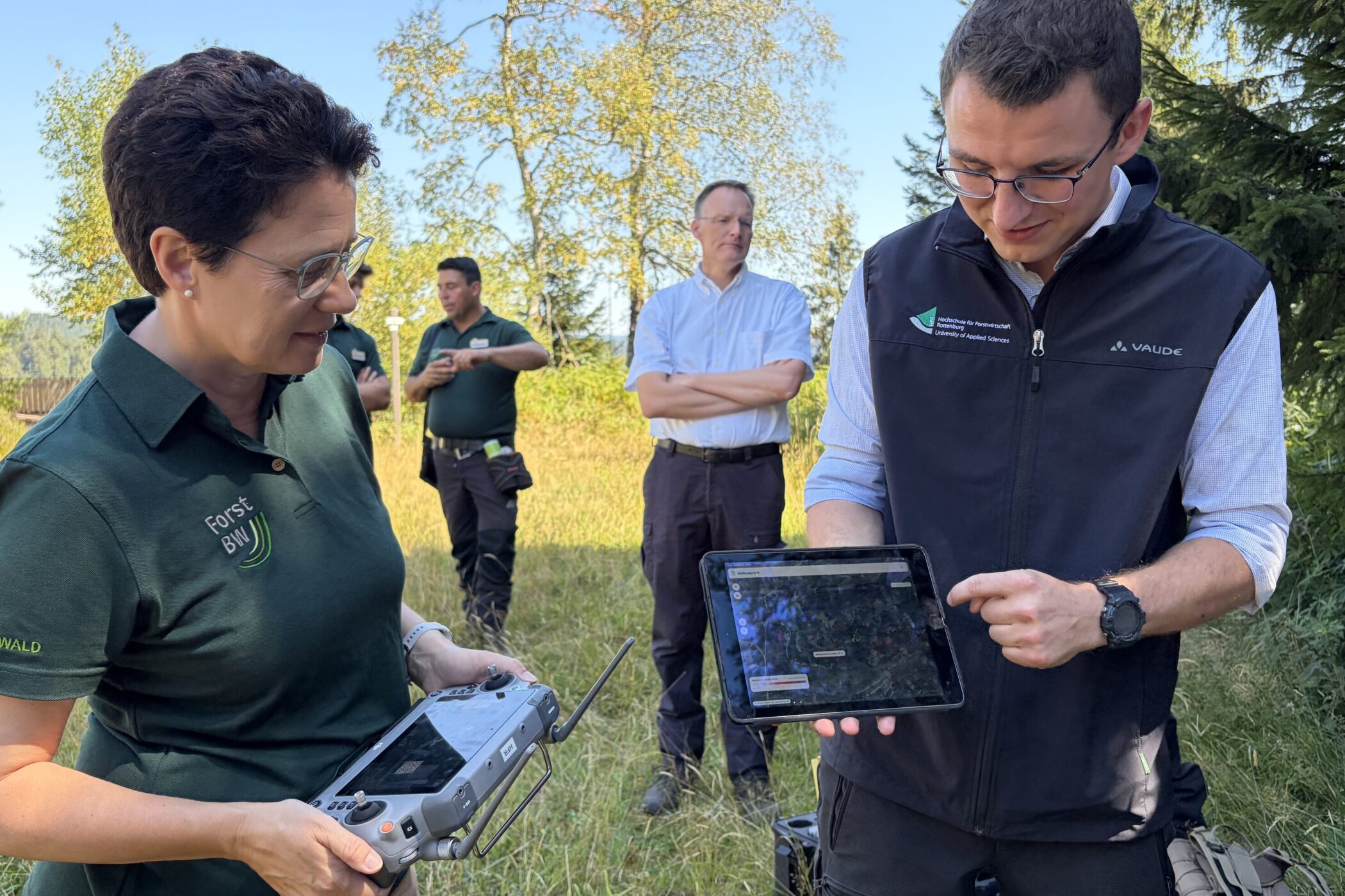 Fünf Personen im Freien, zwei halten ein Tablet und eine Fernbedienung.