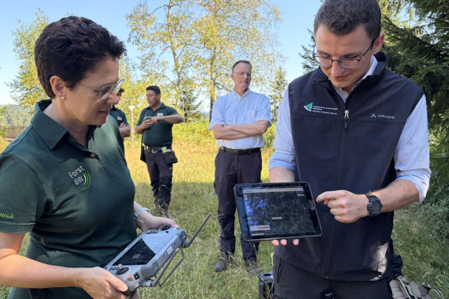 Fünf Personen im Freien, zwei halten ein Tablet und eine Fernbedienung.