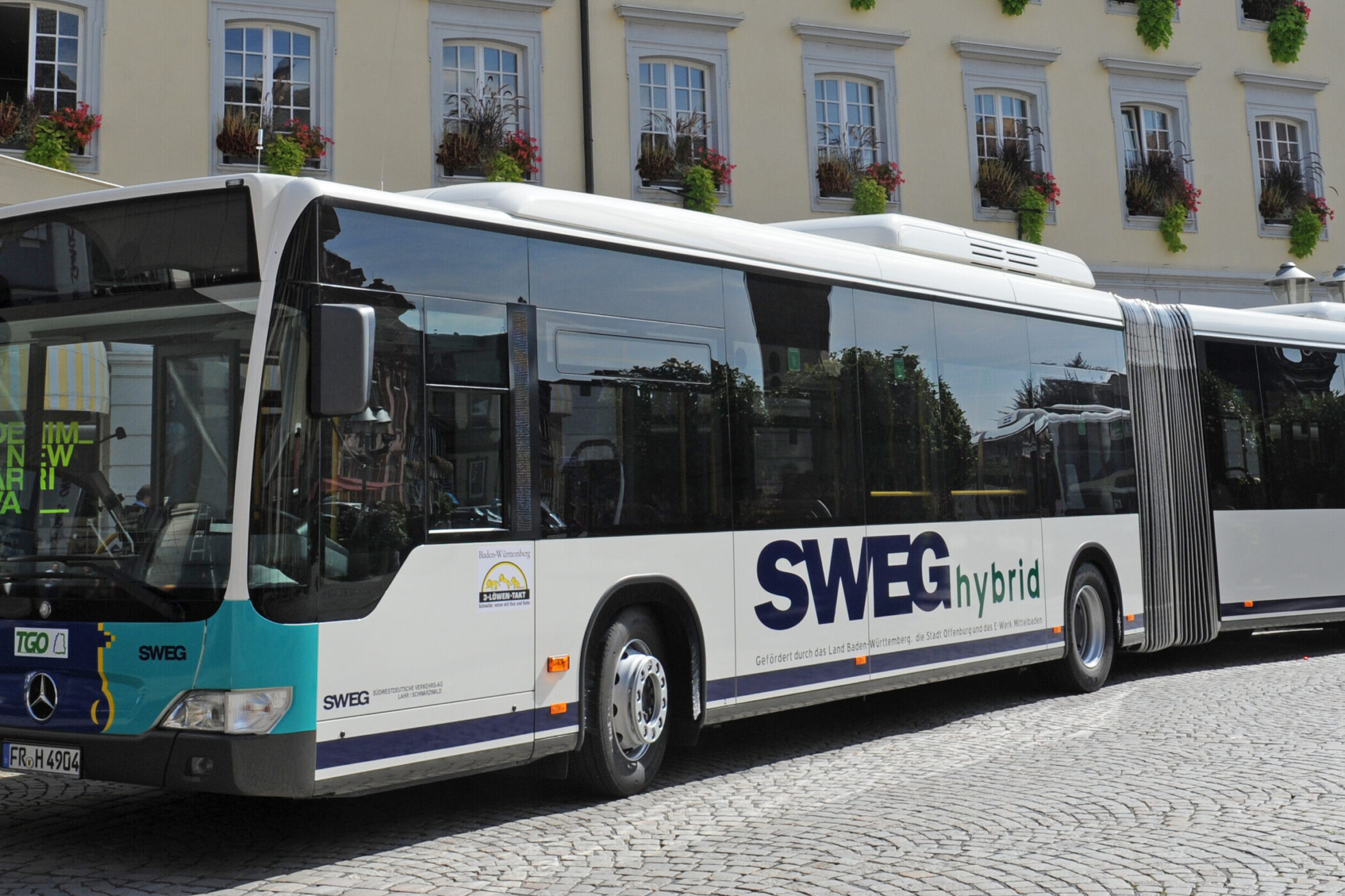 Ein Hybridbus der SWEG auf einem gepflasterten Platz, im Hintergrund ein Gebäude.