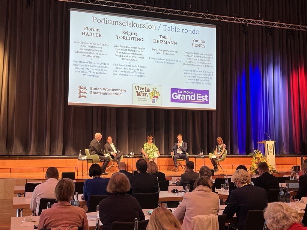 Fünf Personen bei einer Podiumsdiskussion, Publikum vorne.