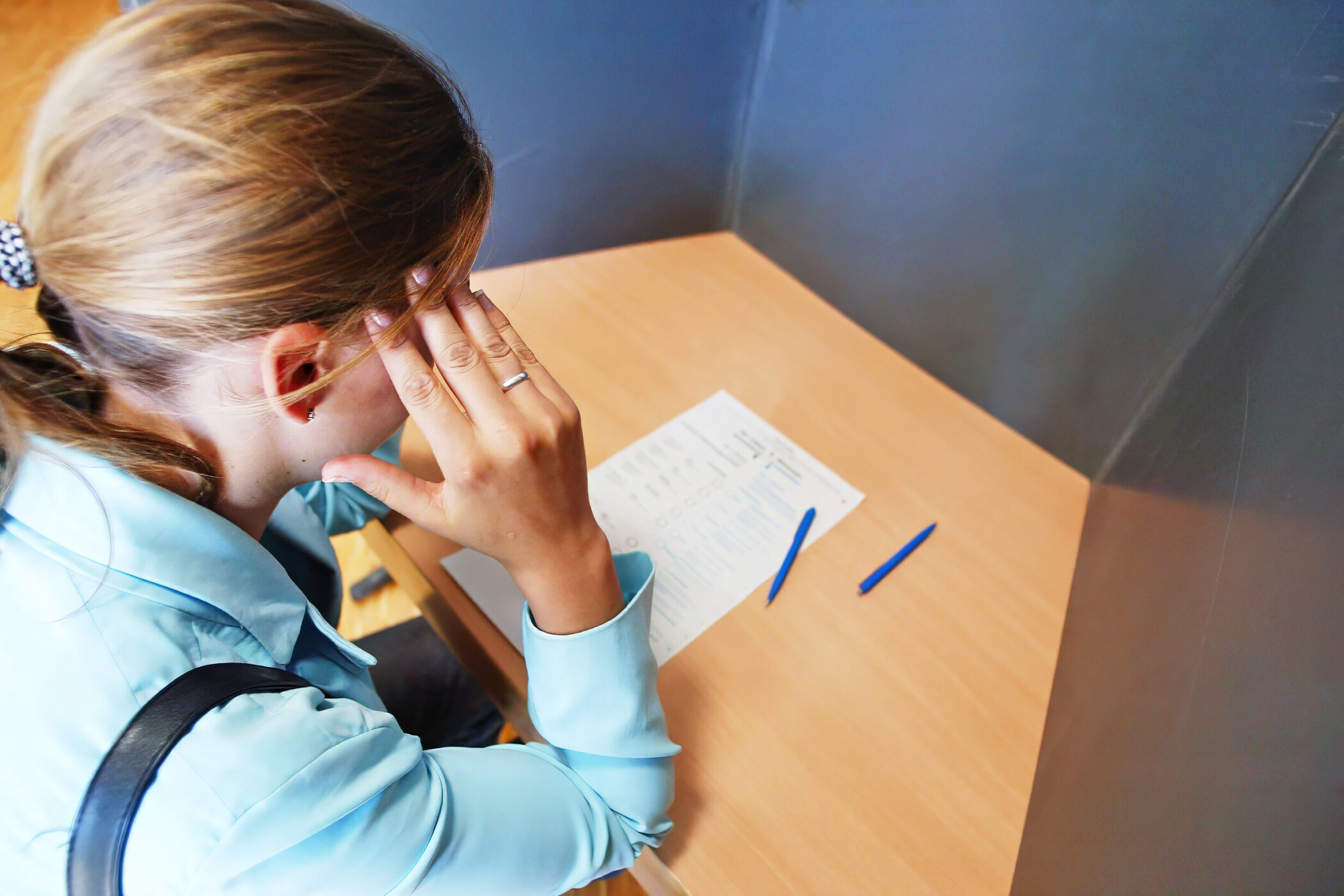 Person am Schreibtisch mit Formular und zwei blauen Stiften.
