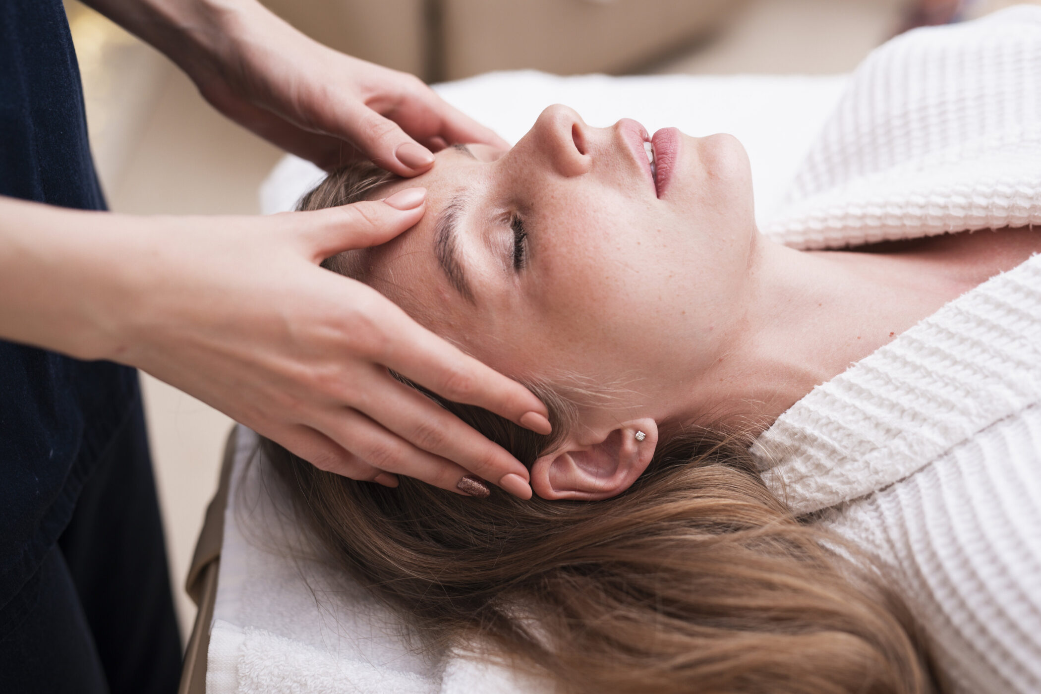 Person erhält Gesichtsmassage, liegt auf weißem Handtuch.