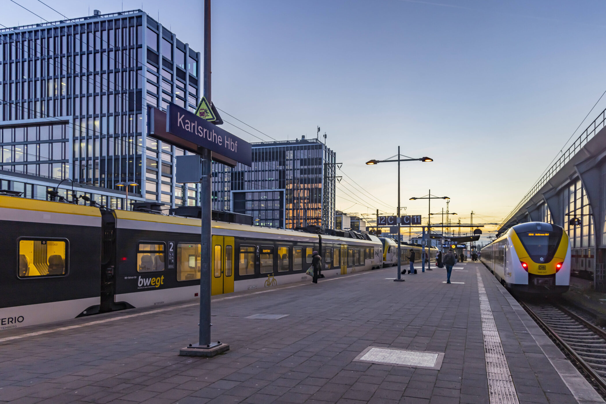 Bahnsteig mit Zügen in Karlsruhe Hbf, Personen gehen entlang des Gleises.