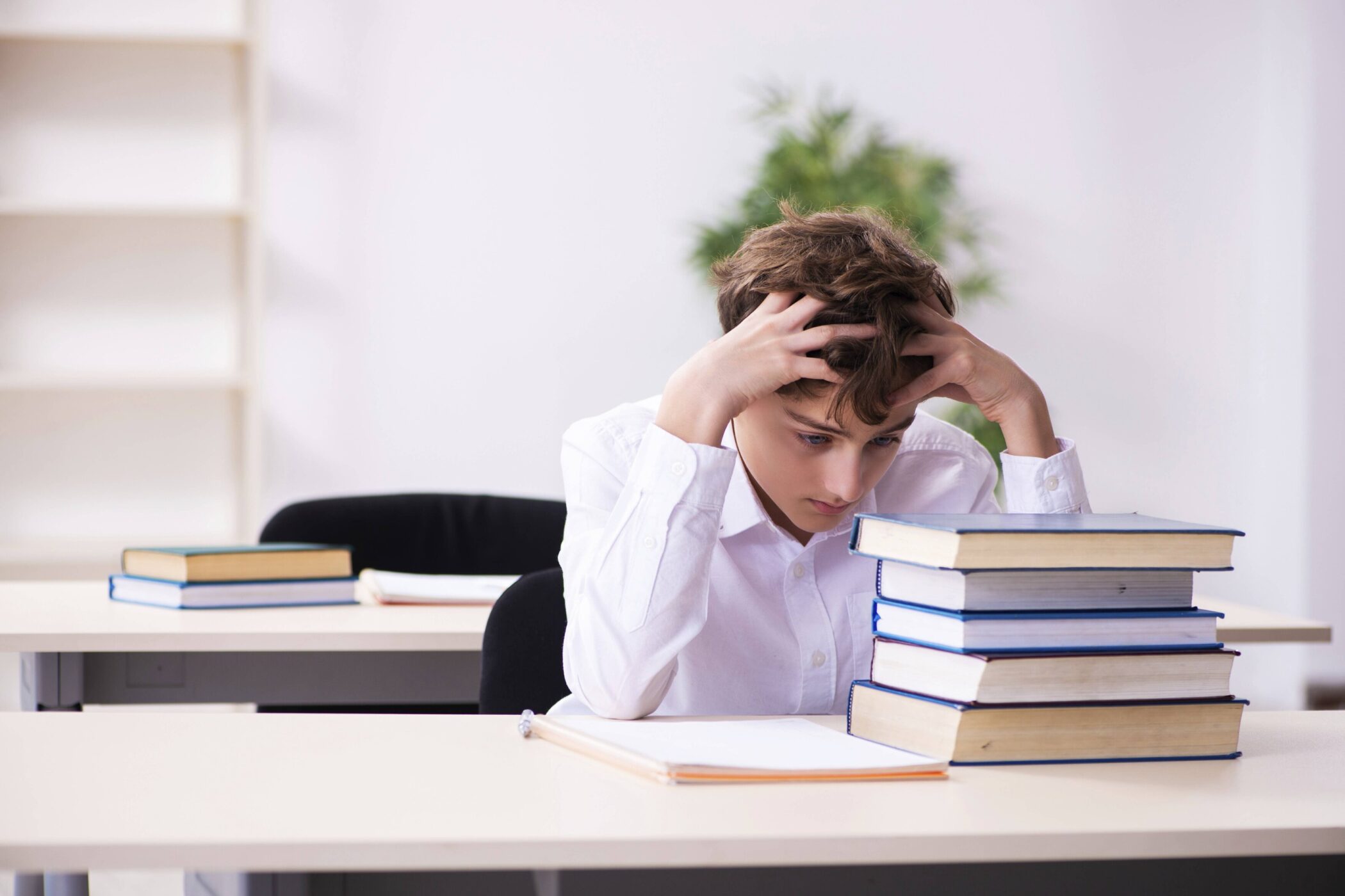 Junge sitzt am Tisch mit Büchern, hält den Kopf in den Händen.