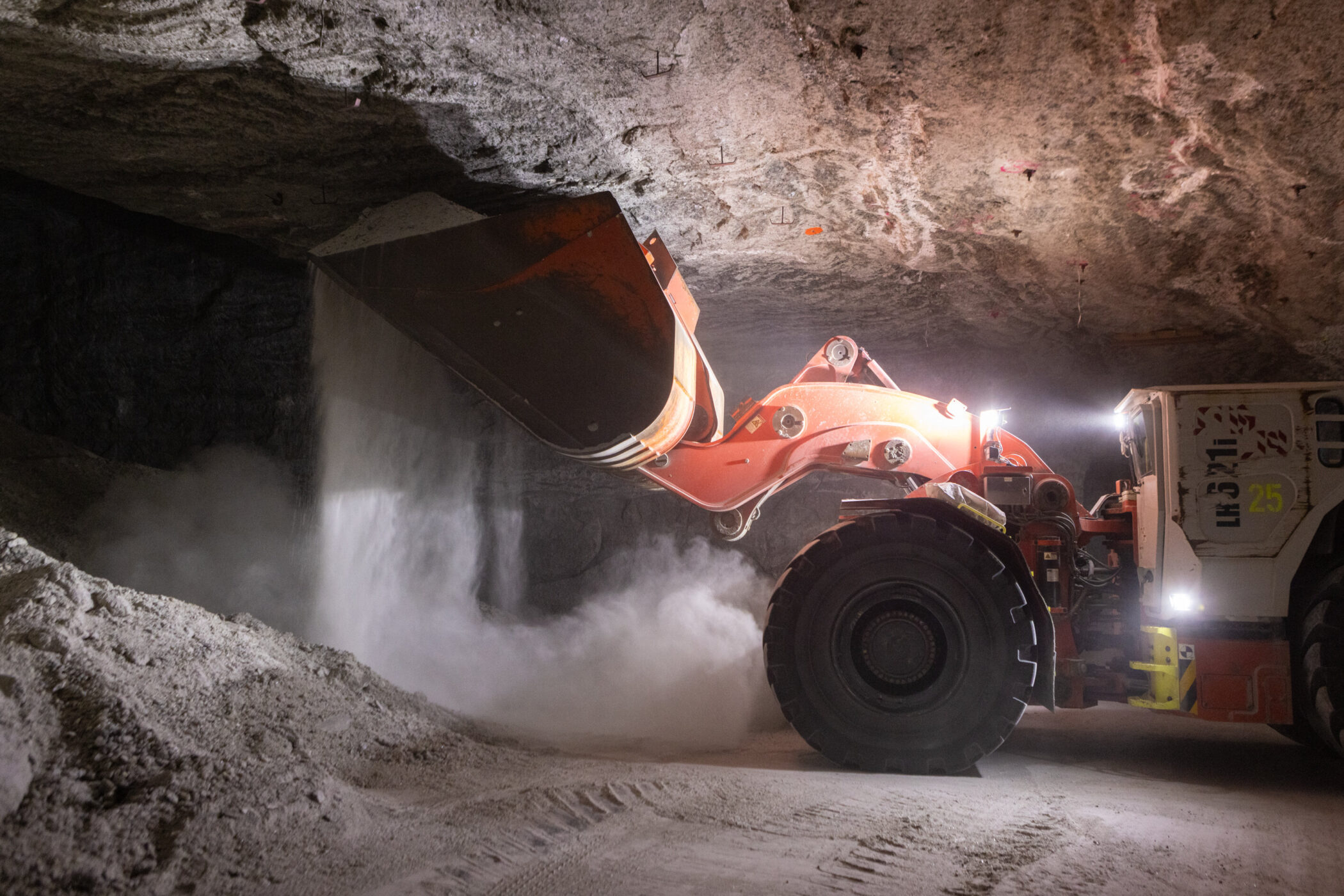 Großer Radlader in Höhle, Schaufel kippt weißes Material auf den Boden.