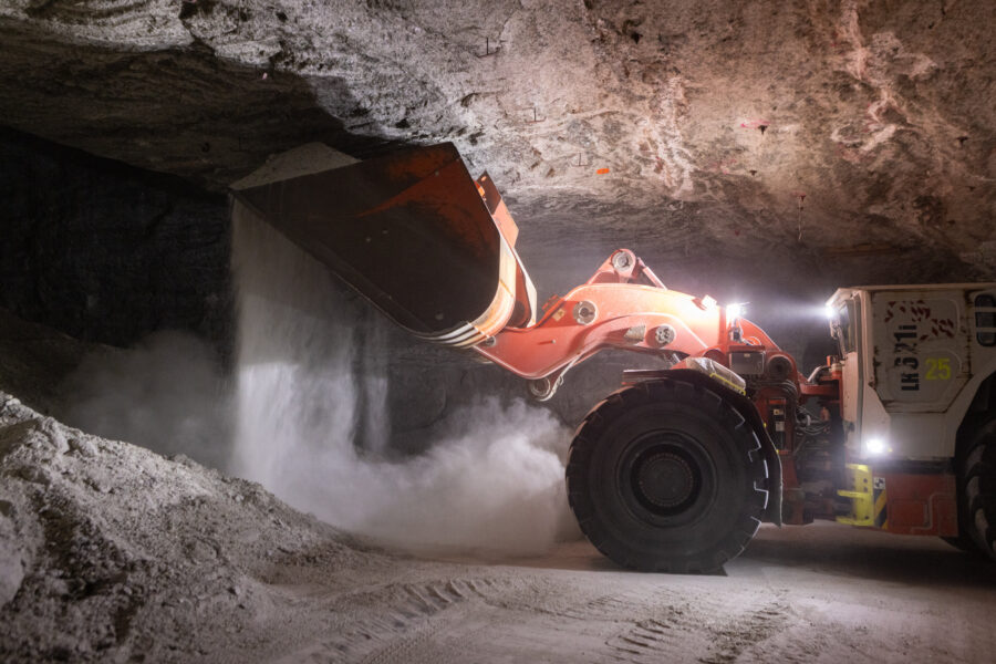 Großer Radlader in Höhle, Schaufel kippt weißes Material auf den Boden.