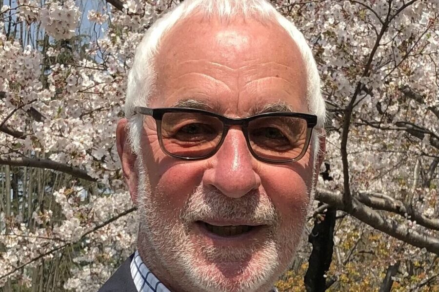 Eine Person mit Brille vor einem blühenden Kirschbaum.