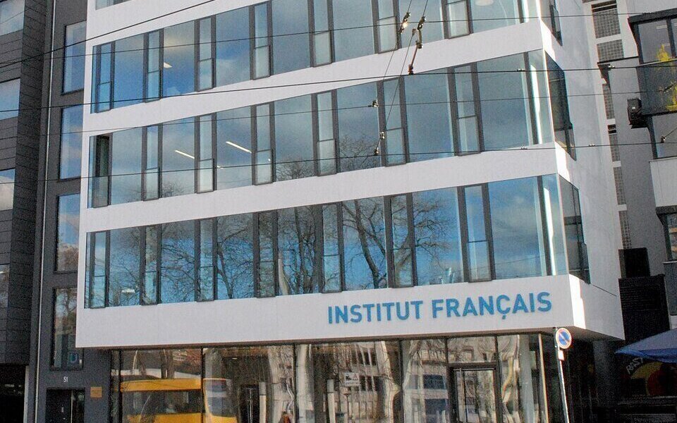 Mehrstöckiges Gebäude mit Schriftzug "INSTITUT FRANÇAIS". Glasfassaden spiegeln Bäume.