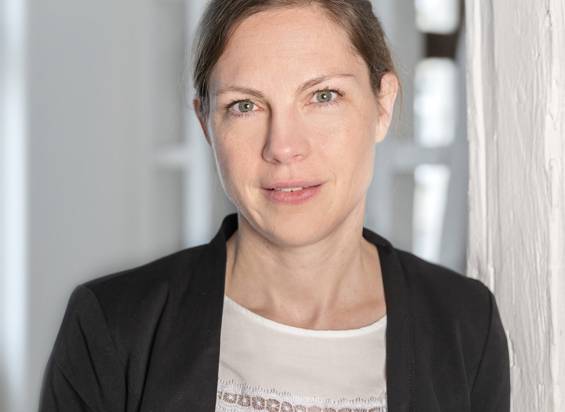Frau mit dunklem Blazer und weißem Oberteil vor weißem Hintergrund.