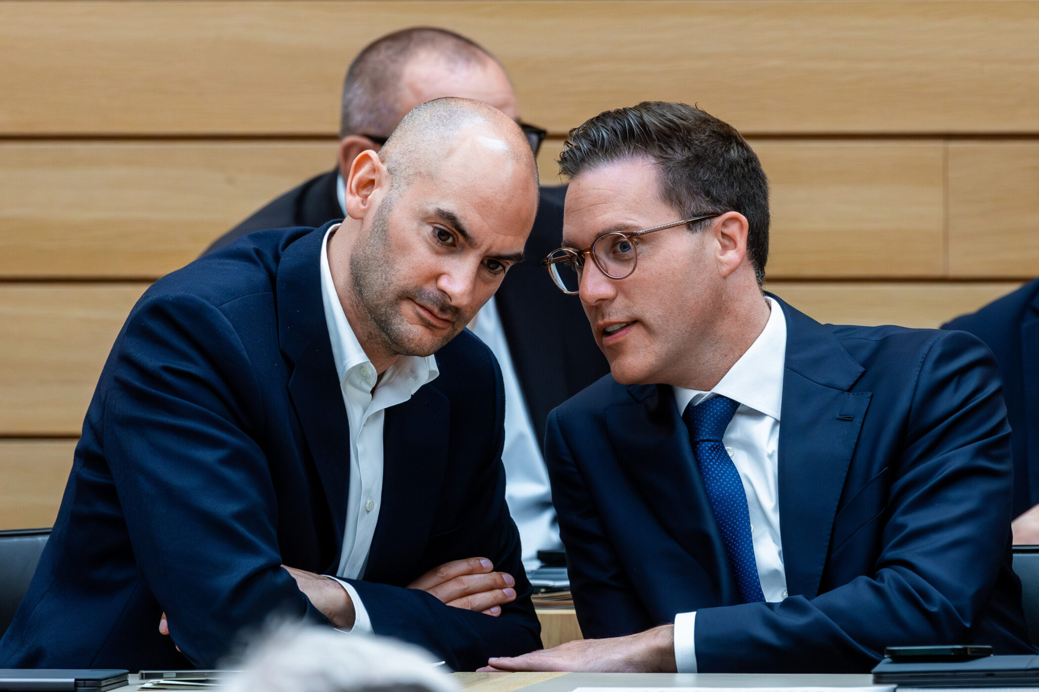 Zwei Männer im Anzug sitzen und sprechen miteinander.