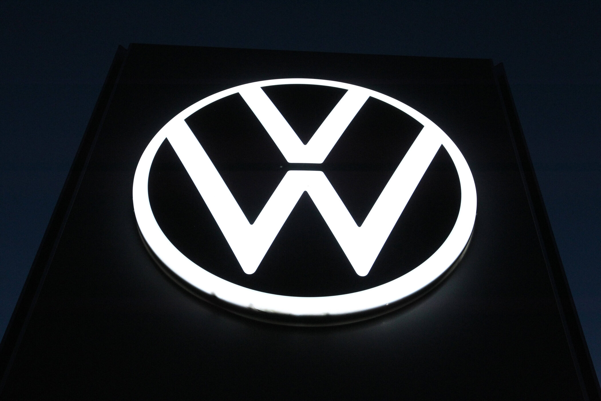 Weiß leuchtendes VW-Logo auf dunklem Hintergrund.