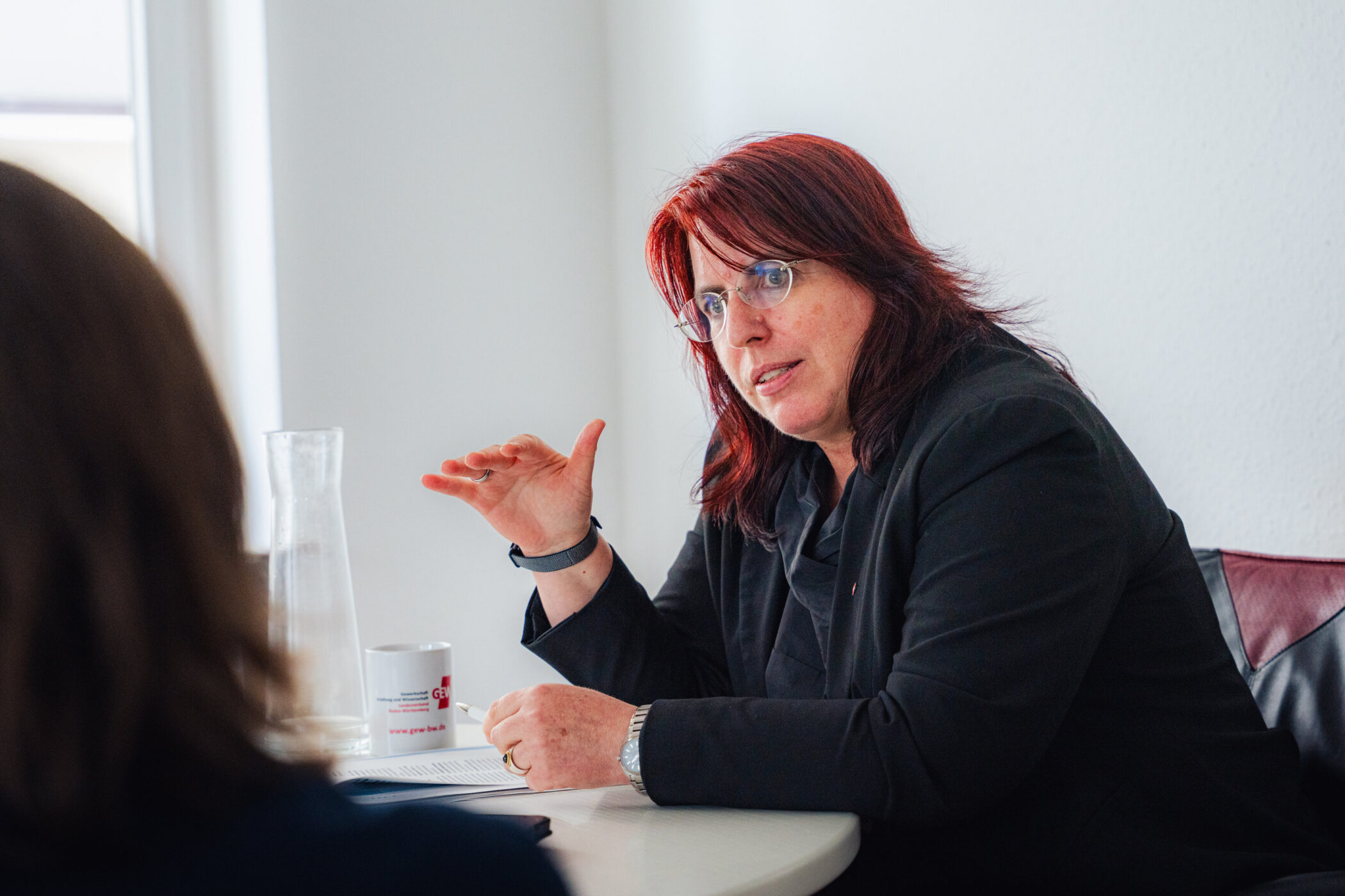 Zwei Personen bei einer Diskussion am Tisch, eine spricht gestikulierend.
