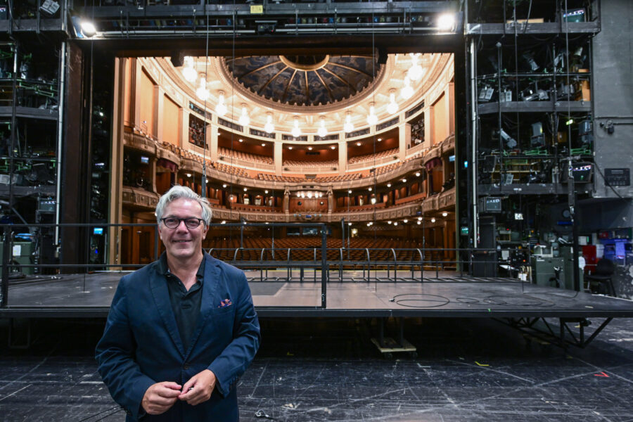 Mann vor Bühne und Theatersitzplätzen, technische Bühnenausrüstung im Hintergrund.