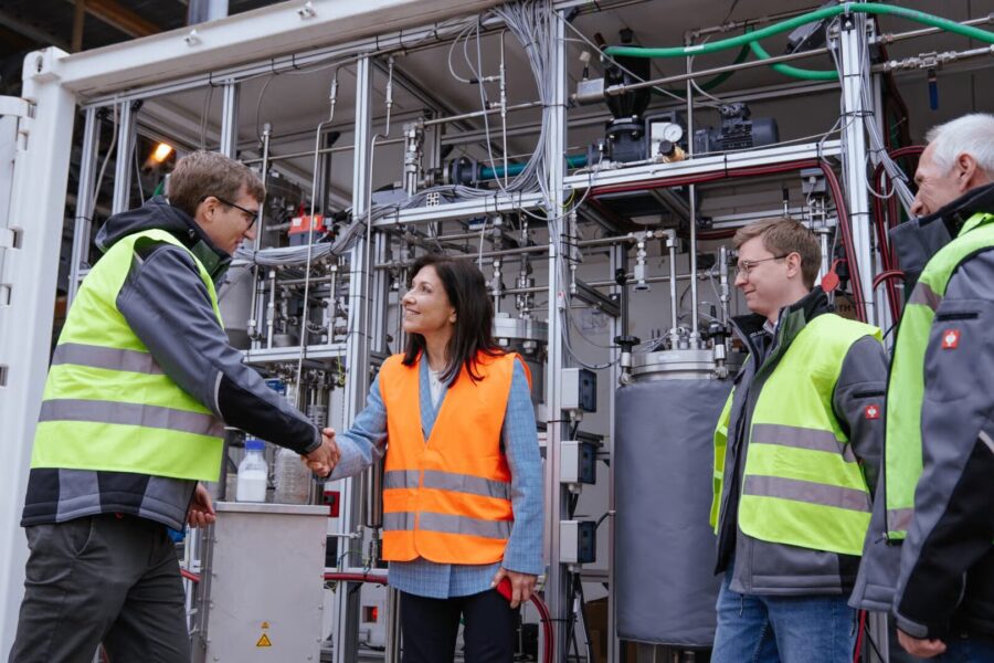 Vier Personen in Warnwesten, Händedruck vor technischer Anlage.