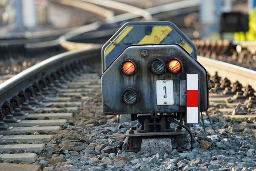 Zwei rote Lichter und eine Tafel mit der Zahl 3 auf Bahngleisen.