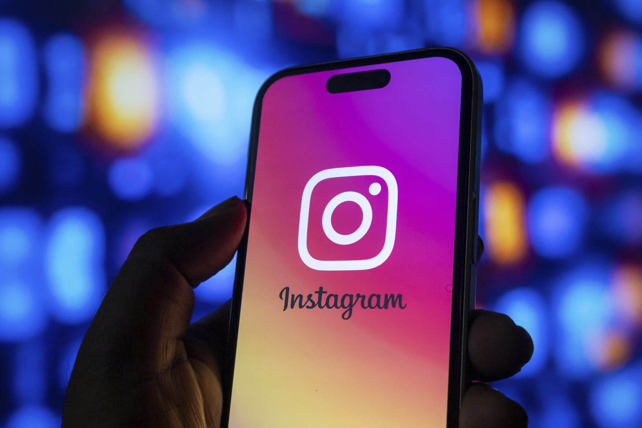 Hand hält Smartphone mit Instagram-Logo, Hintergrund leuchtet blau.