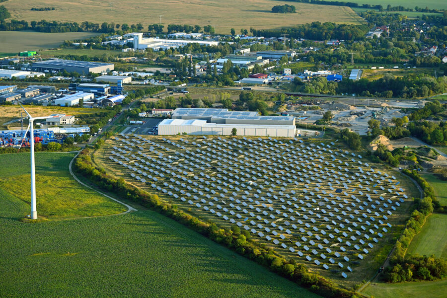 Solaranlage und Windrad auf einem Feld, dahinter Industriegebäude und Felder.