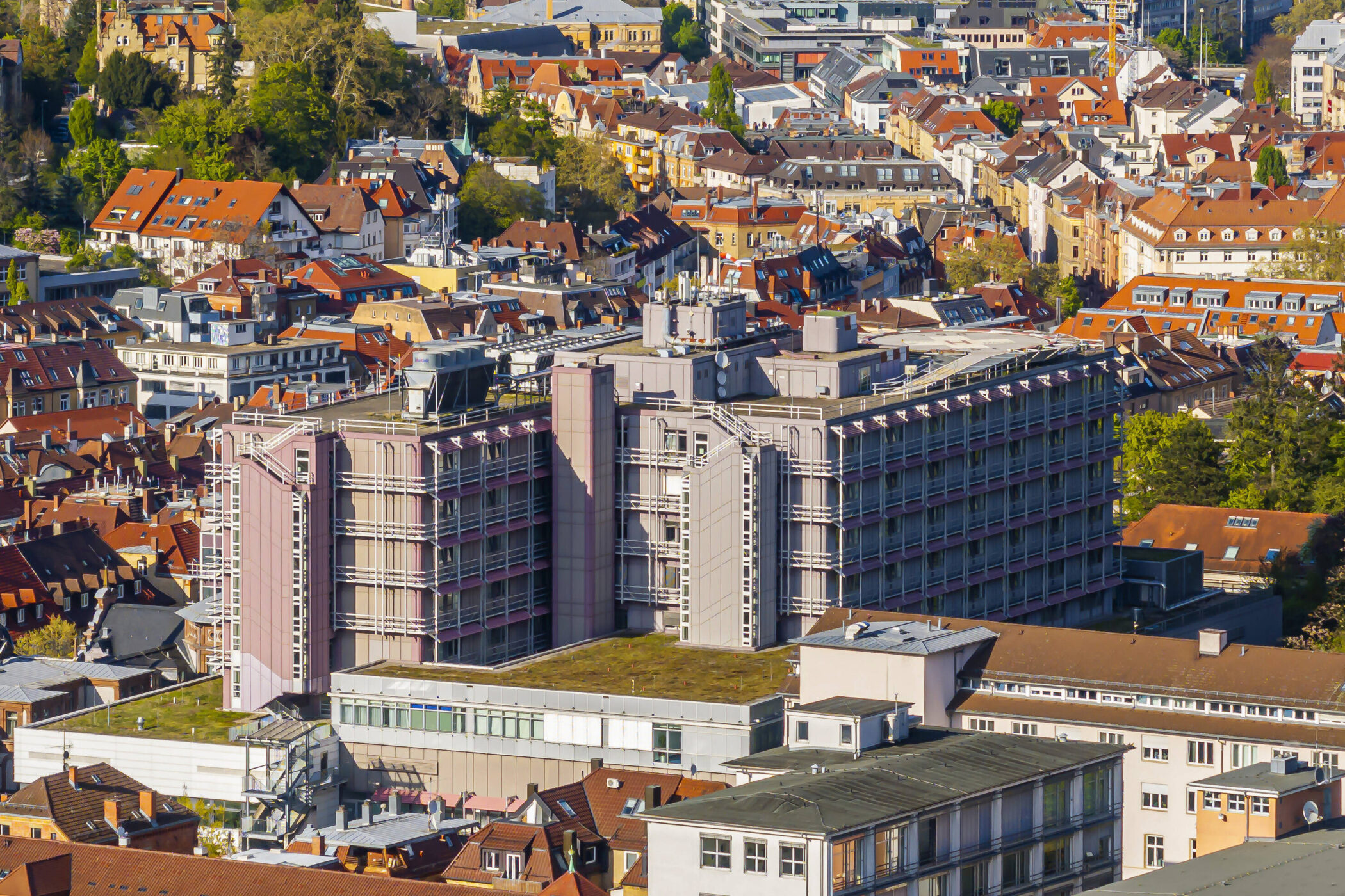 Stadtansicht mit dicht bebauten roten Dächern und einem großen mehrstöckigen Gebäude.