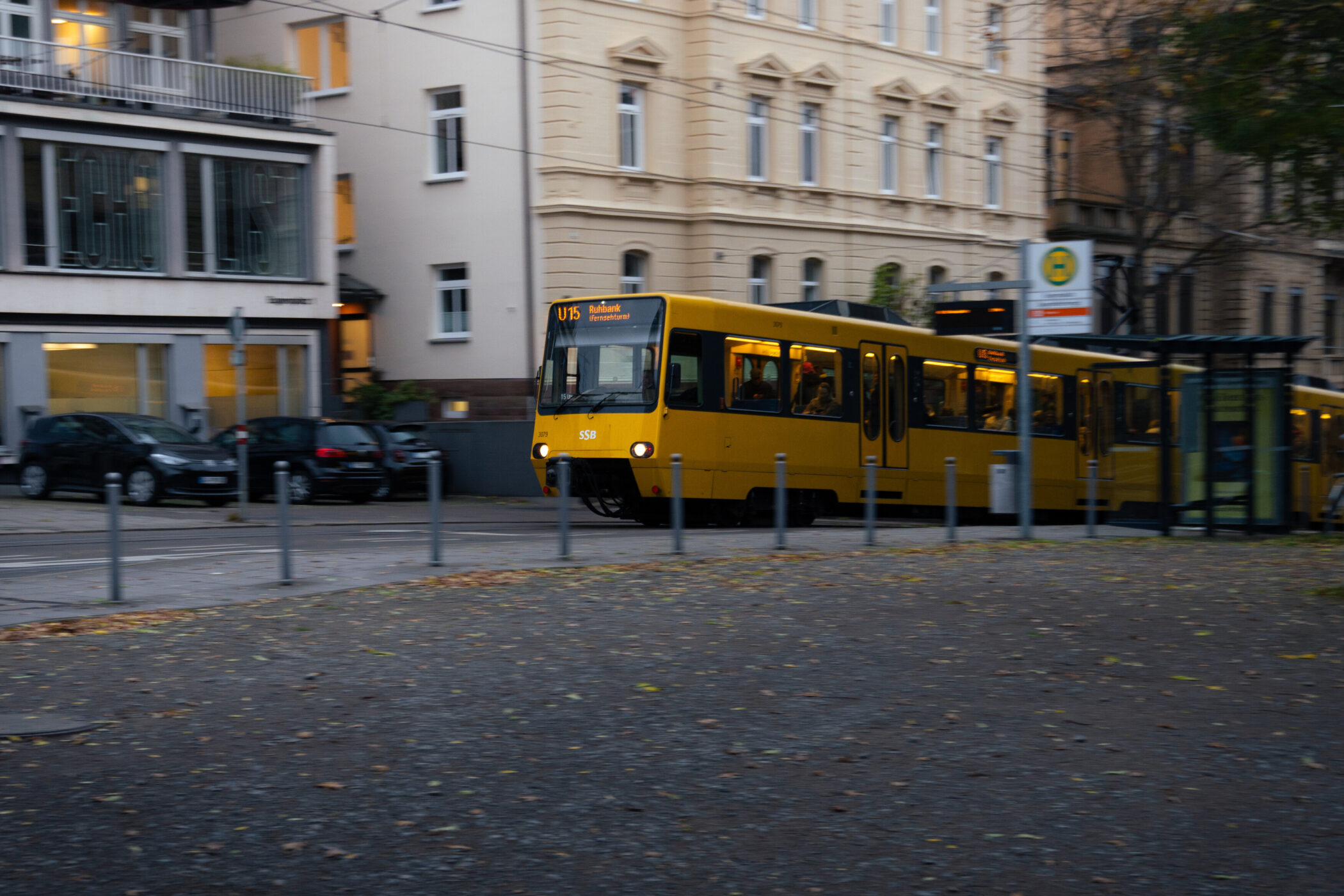 Gelbe Straßenbahn der Linie U15 an Haltestelle vor Wohnhäusern und geparkten Autos.