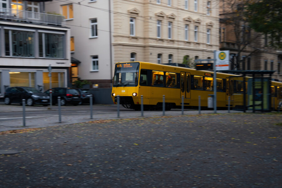 Gelbe Straßenbahn der Linie U15 an Haltestelle vor Wohnhäusern und geparkten Autos.
