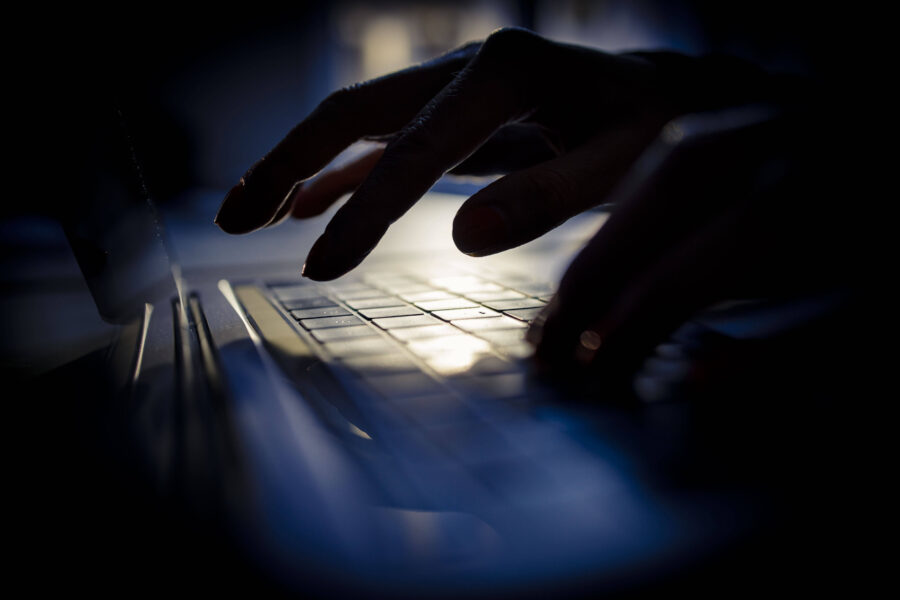 Hand tippt auf Laptop-Tastatur im Dunkeln.