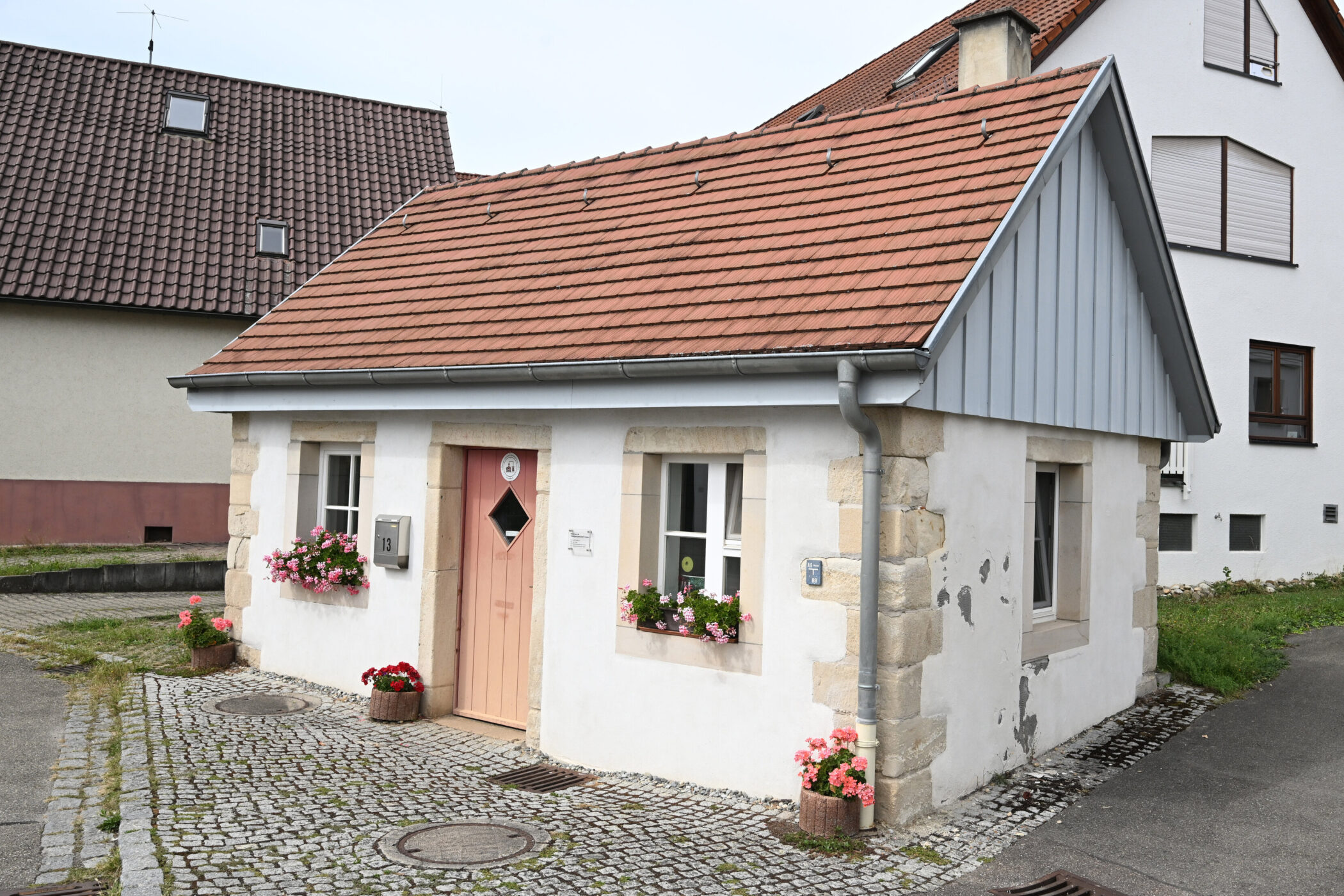 Kleines weißes Haus mit rotem Dach, Blumen in Kästen, Hausnummer 13.