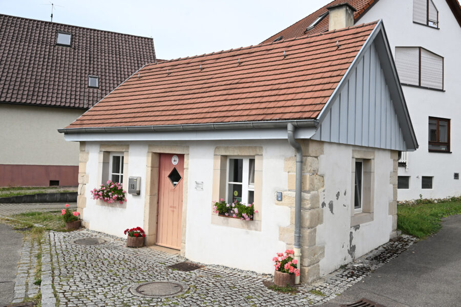 Kleines weißes Haus mit rotem Dach, Blumen in Kästen, Hausnummer 13.
