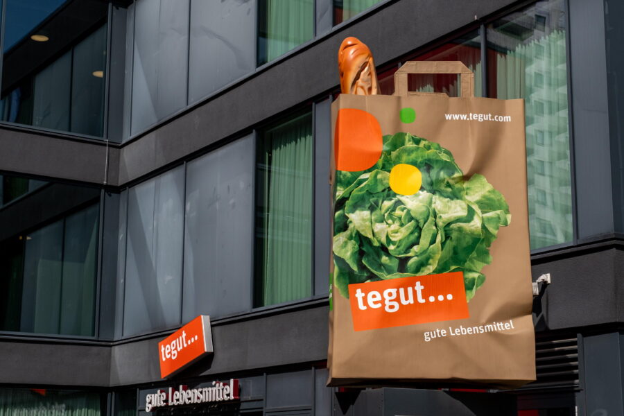 Braune Tüte mit Kopfsalat und Baguette außen an Gebäude, Aufschrift: tegut…
