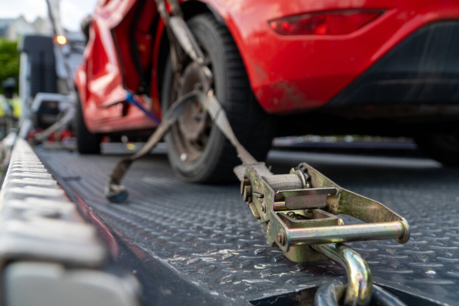 Rotes Auto wird mit Gurten auf einem Abschleppwagen gesichert.