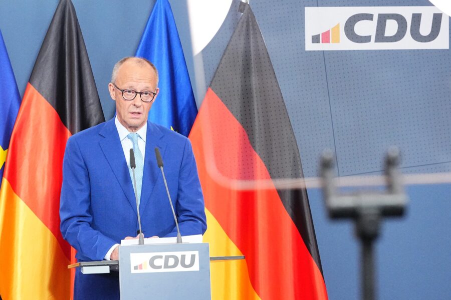 Mann am Rednerpult mit CDU-Logo, drei Flaggen im Hintergrund.