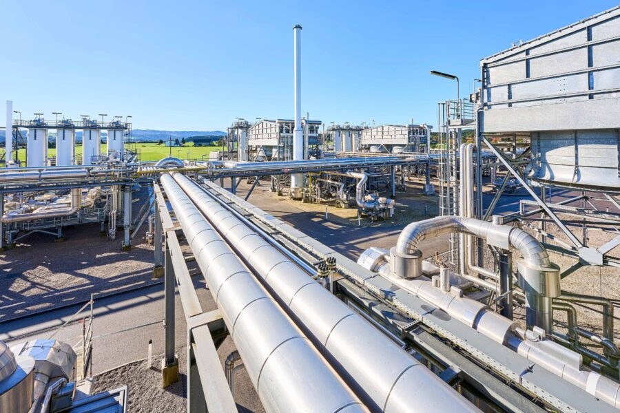 Industrierohre und -tanks im Freien, grüne Felder im Hintergrund.