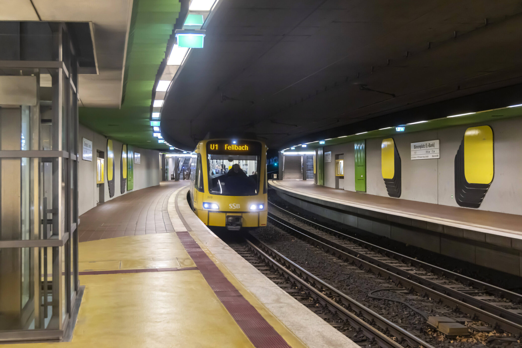 Zug U1 Fellbach in U-Bahn-Station, leere Bahnsteige, gelb-grünes Design.