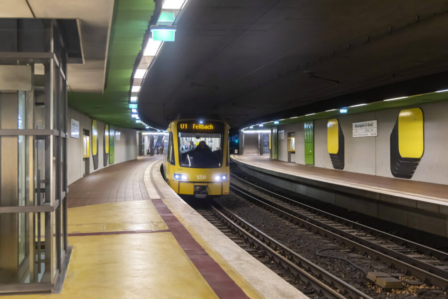 Zug U1 Fellbach in U-Bahn-Station, leere Bahnsteige, gelb-grünes Design.