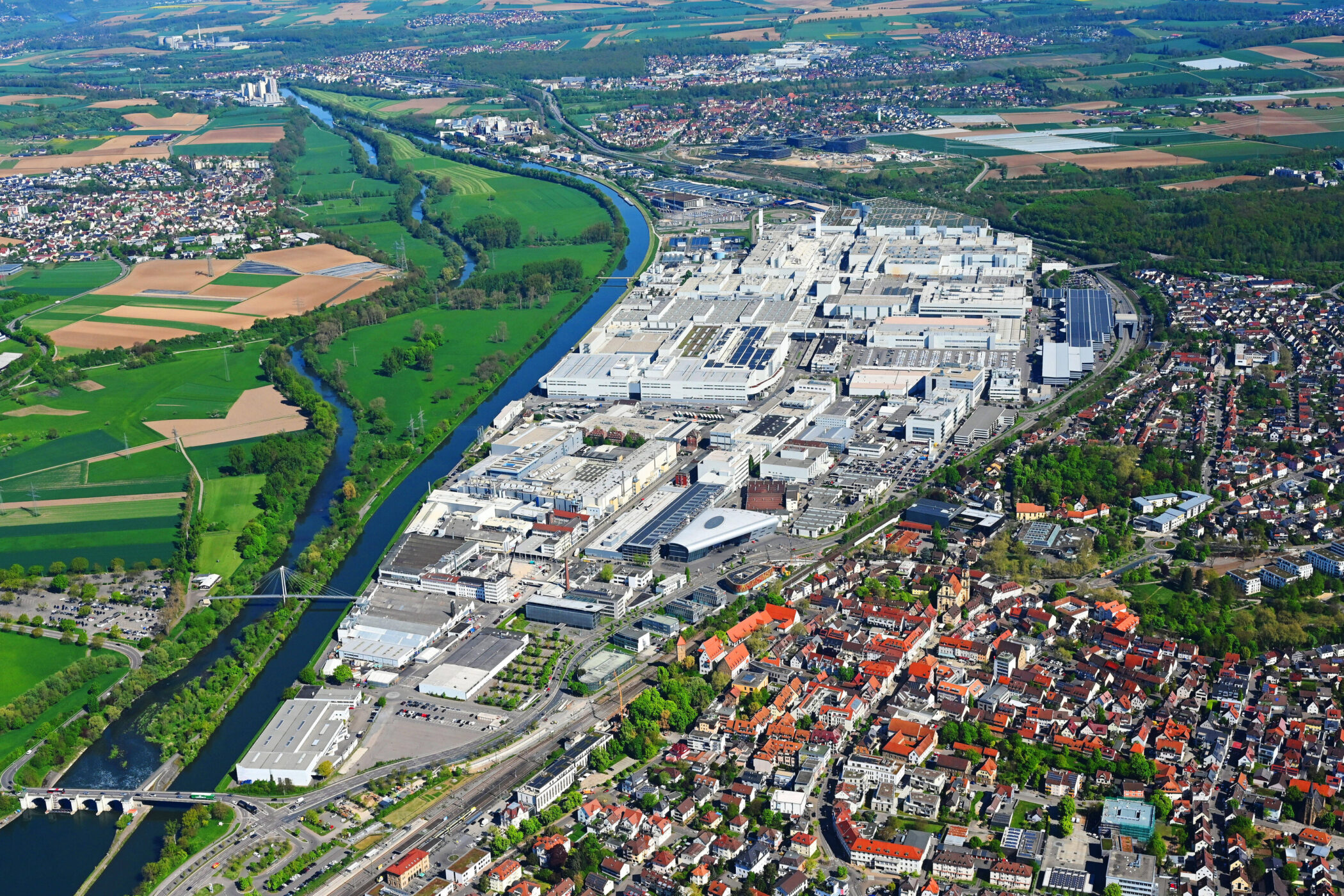 Stadtansicht mit Wohngebäuden, Fabrikkomplex und blauem Fluss im Grünen.