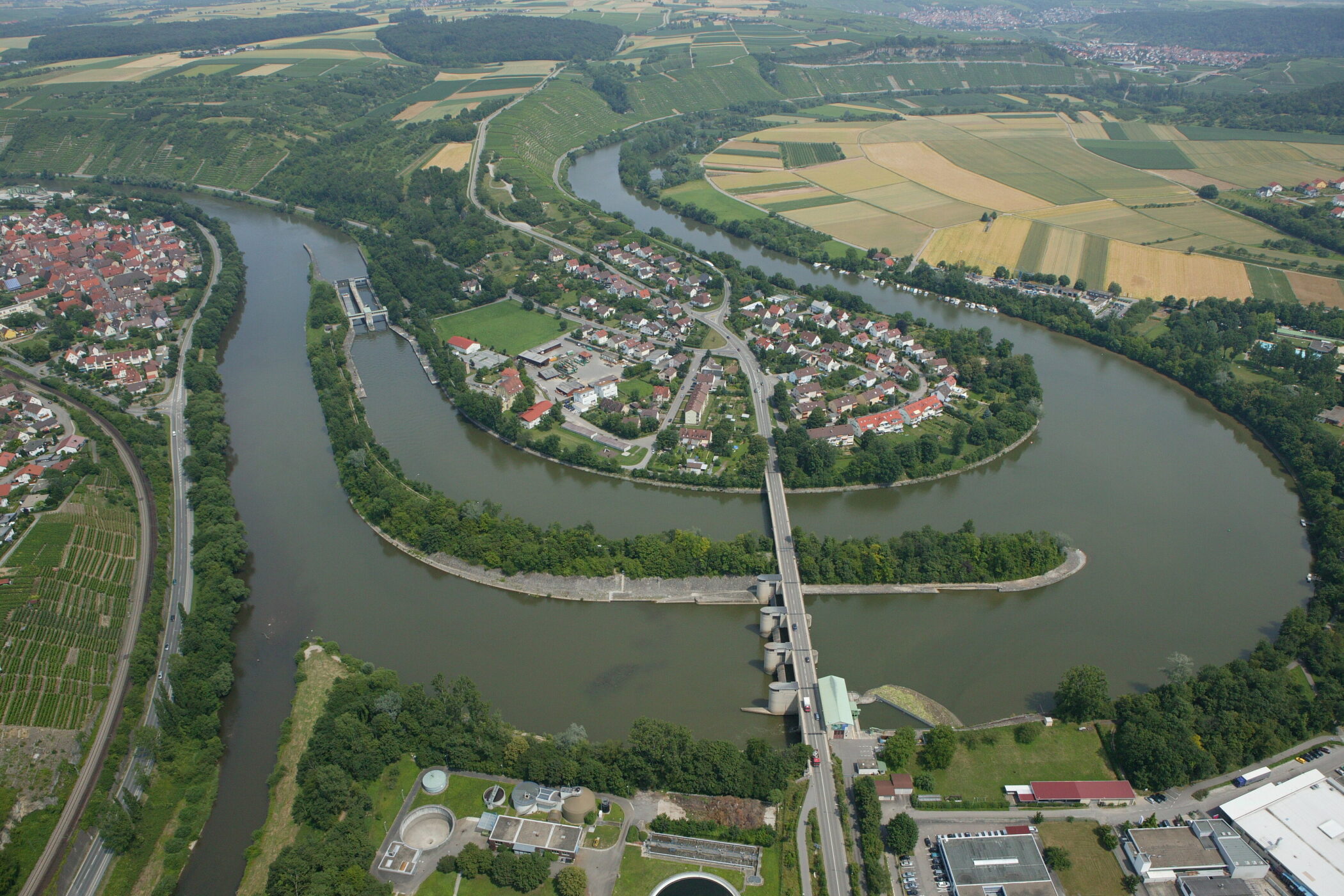 Luftbild einer Flusslandschaft mit Schleuse, Brücke und umliegenden Gebäuden.