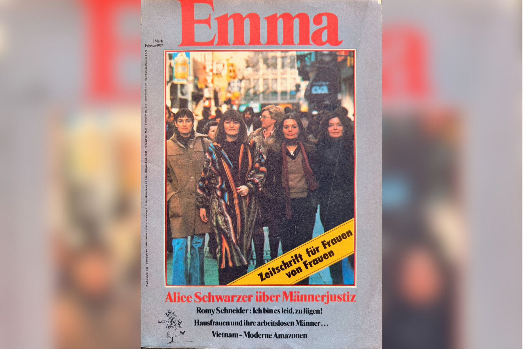 Vier Frauen gehen in einer belebten Straße; Schriftzug „Emma“ oben.