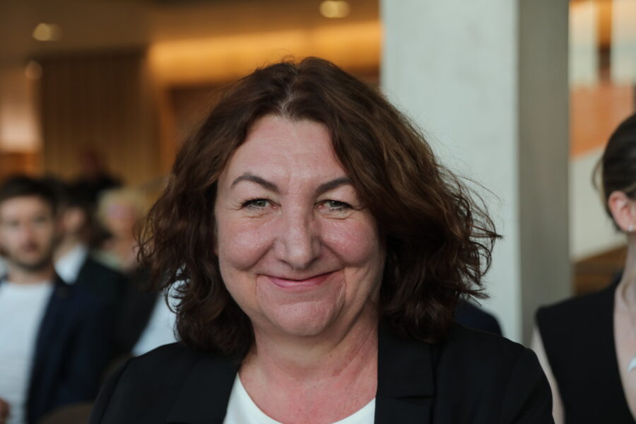 Eine Frau lächelt, verschwommene Menschen im Hintergrund.