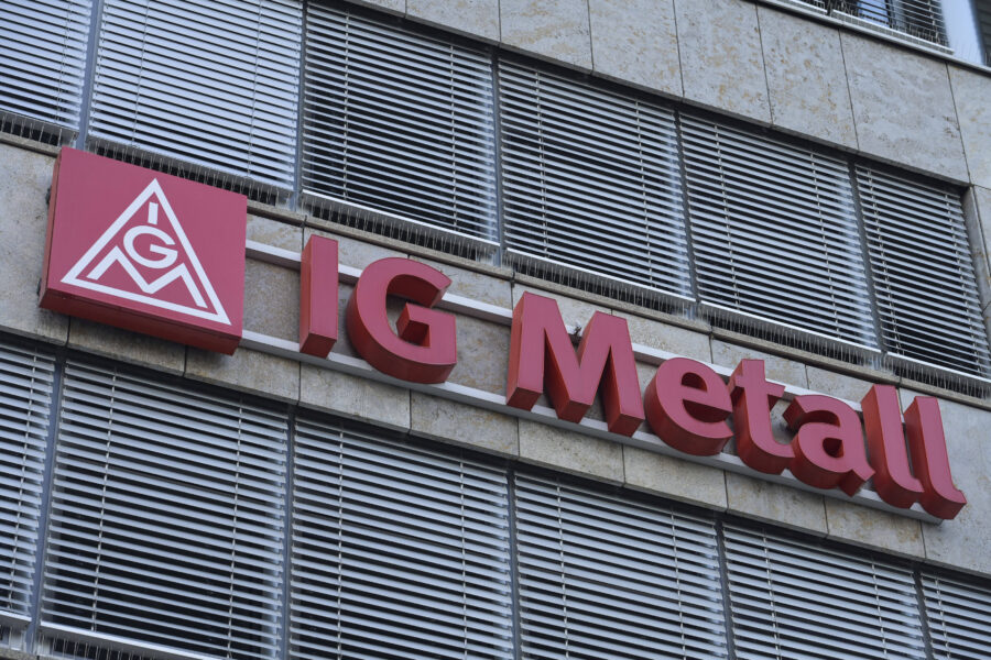 Rotes Logo und Schriftzug "IG Metall" an Gebäudewand, Fenster mit Jalousien.