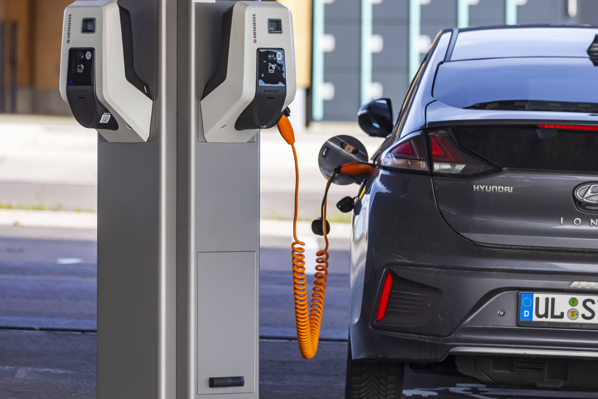 E-Auto lädt an grauer Ladesäule mit orangem Kabel.