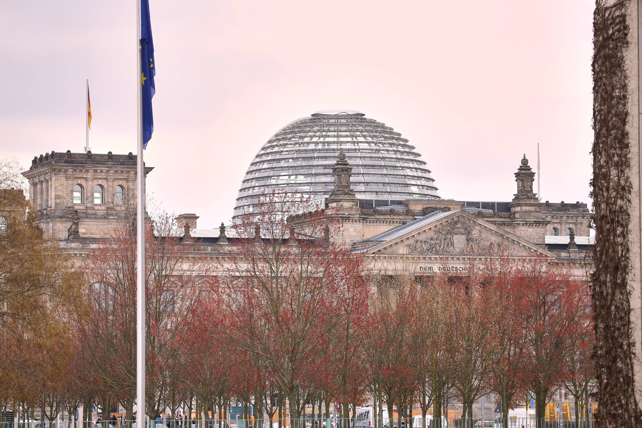 Gebäude mit Glaskuppel und Fahnenmast, Bäume im Vordergrund.