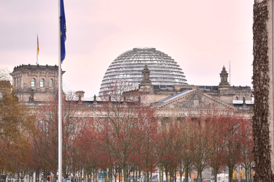 Gebäude mit Glaskuppel und Fahnenmast, Bäume im Vordergrund.